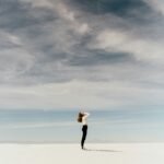 woman looking up to the sky while standing on white sand